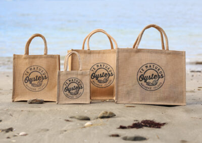 A collection of jute bags, featuring a business logo. Professional product photography in an outdoor beach setting. Content and product photography in Auckland, New Zealand.