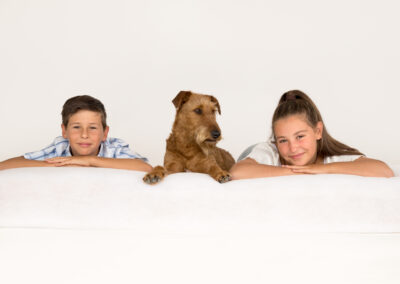 Happy family photo with siblings and their pet dog, taken in a professional portrait studio. Siblings portrait photography in Auckland featuring smiling daughter, son & irish terrier pet dog.