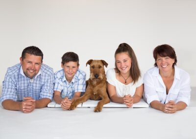 Happy family photo with their pet dog, taken in a professional portrait studio. Family photography in Auckland featuring mum, dad, daughter, son & irish terrier pet dog.