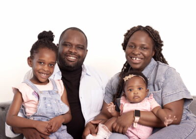 In Home Family Portrait of Mum, Dad, Baby girl and Daughter smiling on the sofa.