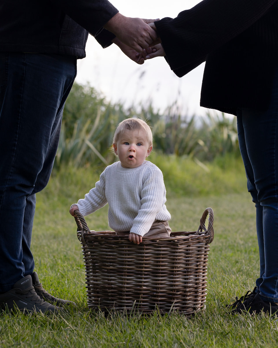 parents silhouette standing over baby in basket on grass