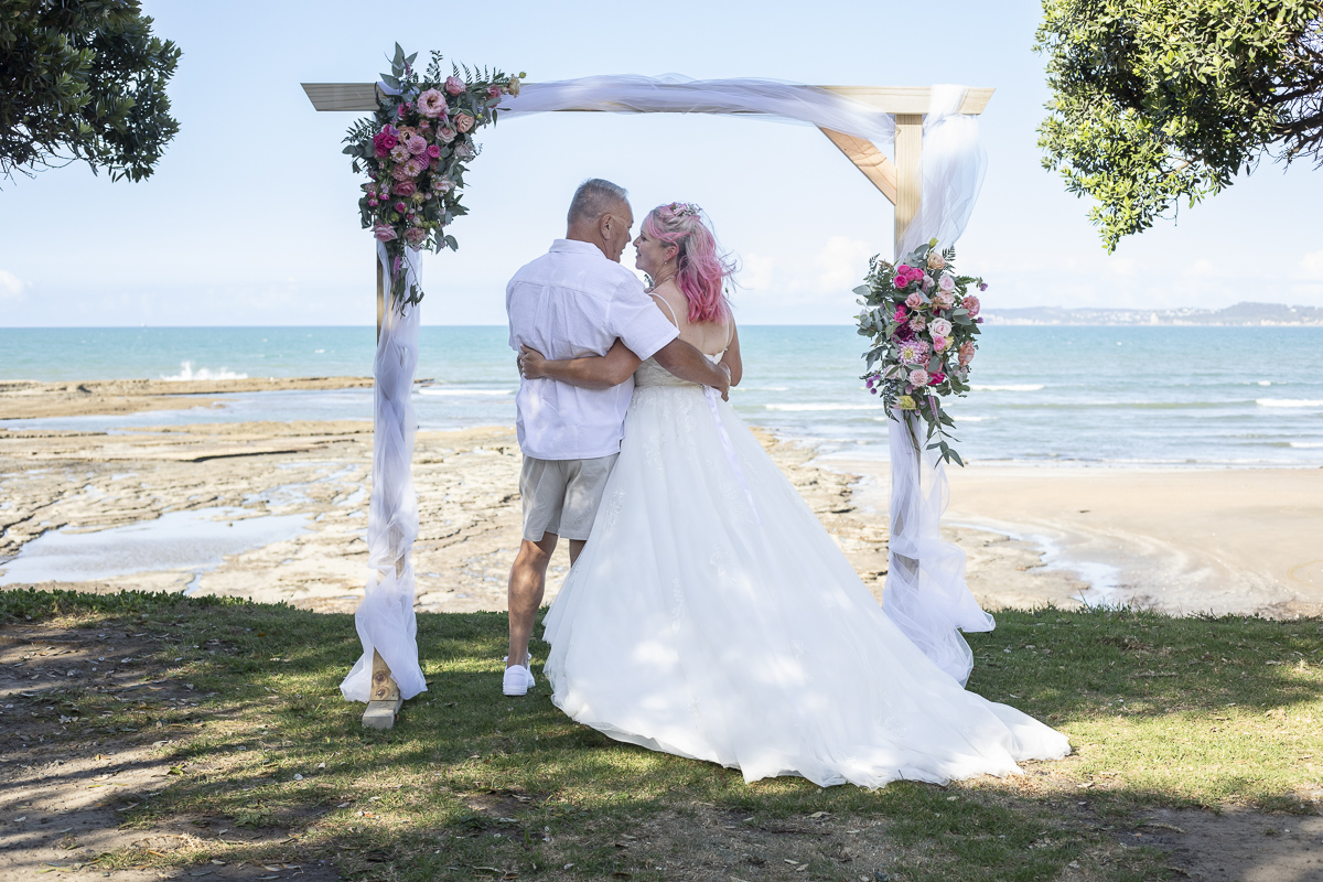Mature wedding couple standing under arch on beach front